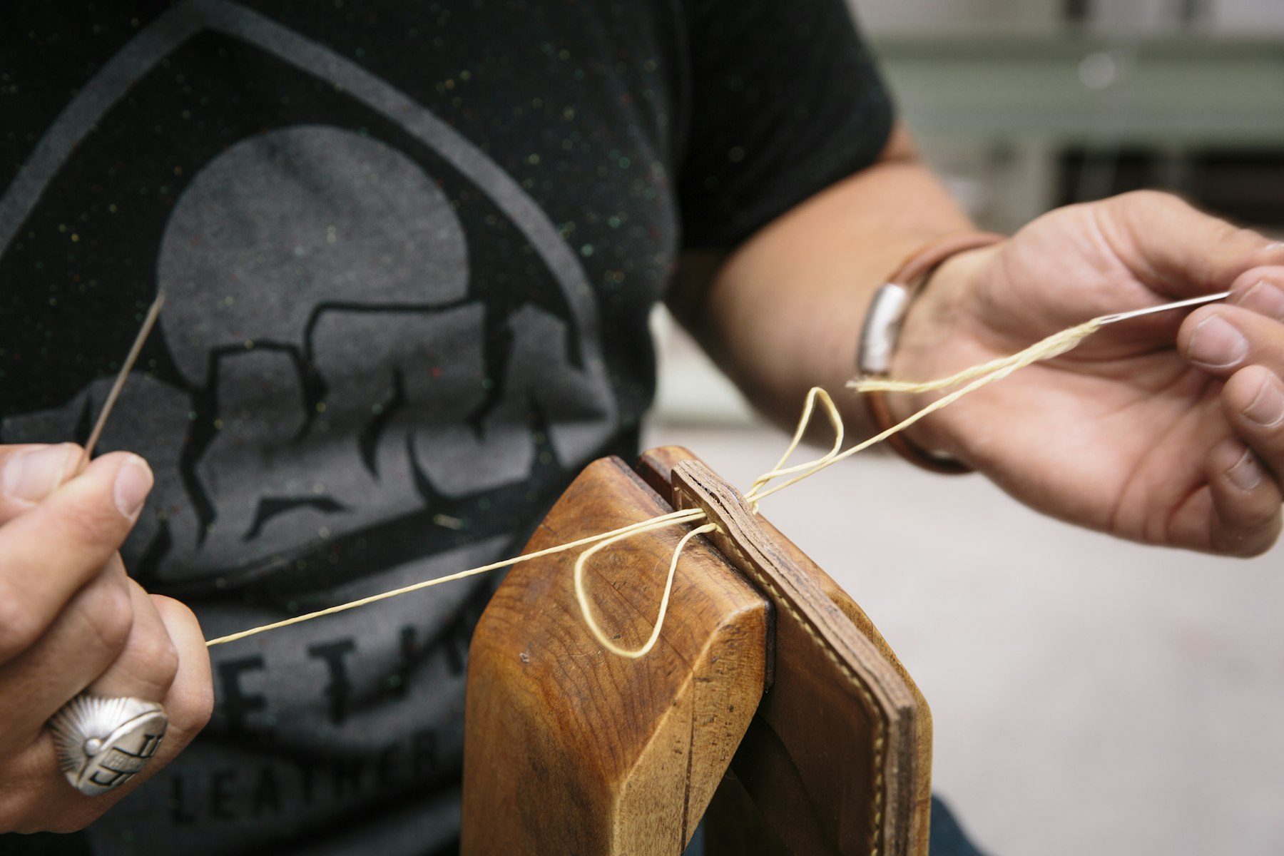 Mains d’artisan qui recousent l’anse d’un sac en cuir