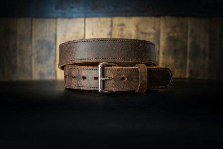 Ceinture homme en cuir marron pleine fleur avec boucle ardillon, pliée sur un fond neutre