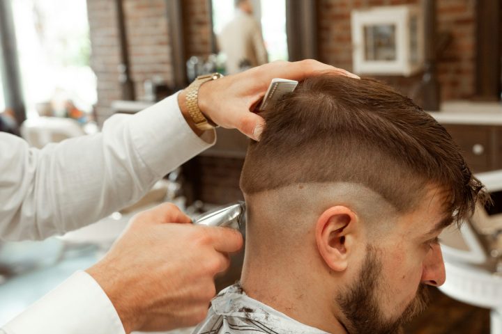 Barbier en train de tailler le dégradé d'une coupe homme dans un barbershop.