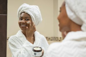 Femme appliquant une crème de soin devant un miroir